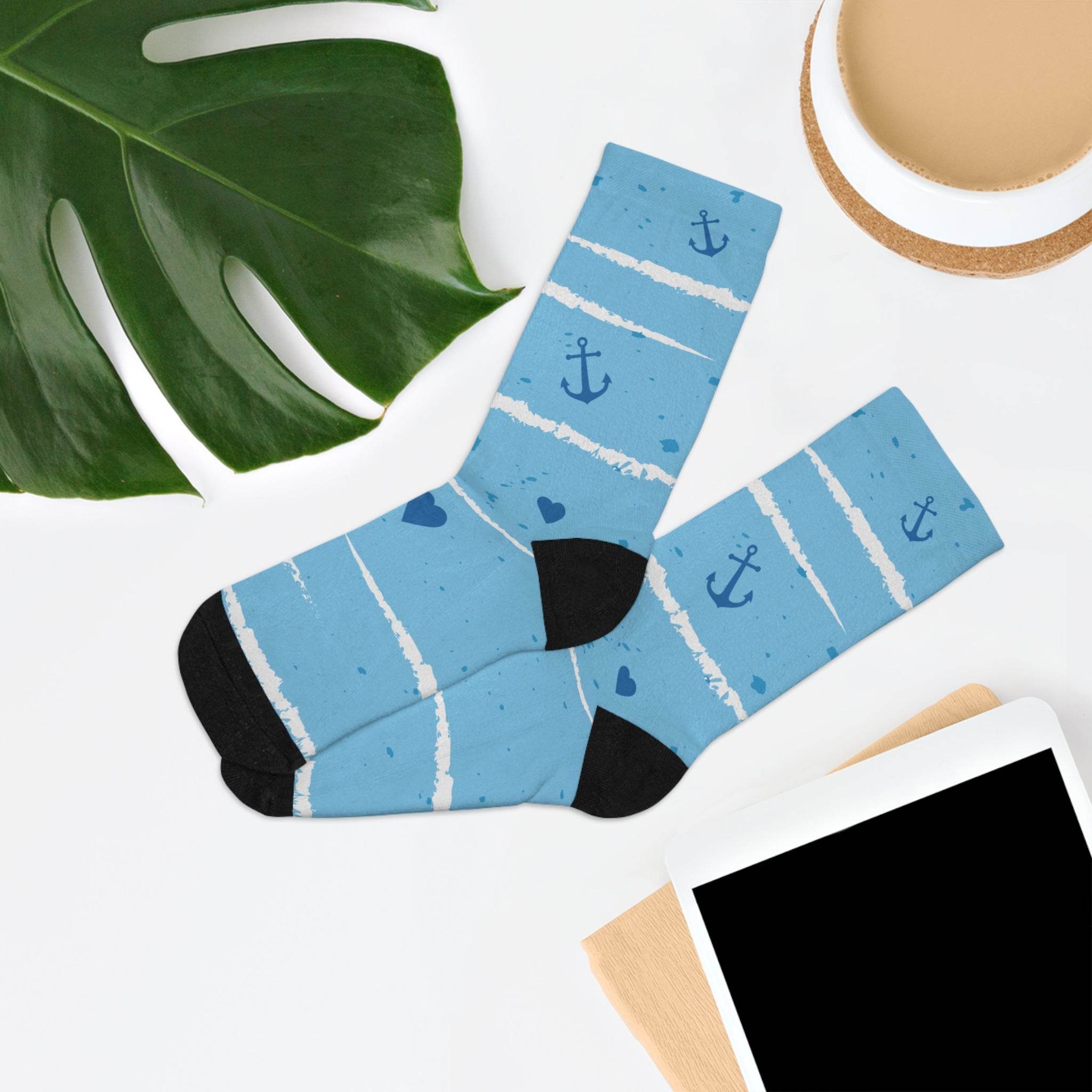 Blue recycled poly socks with anchor and heart patterns displayed next to a green leaf and tablet