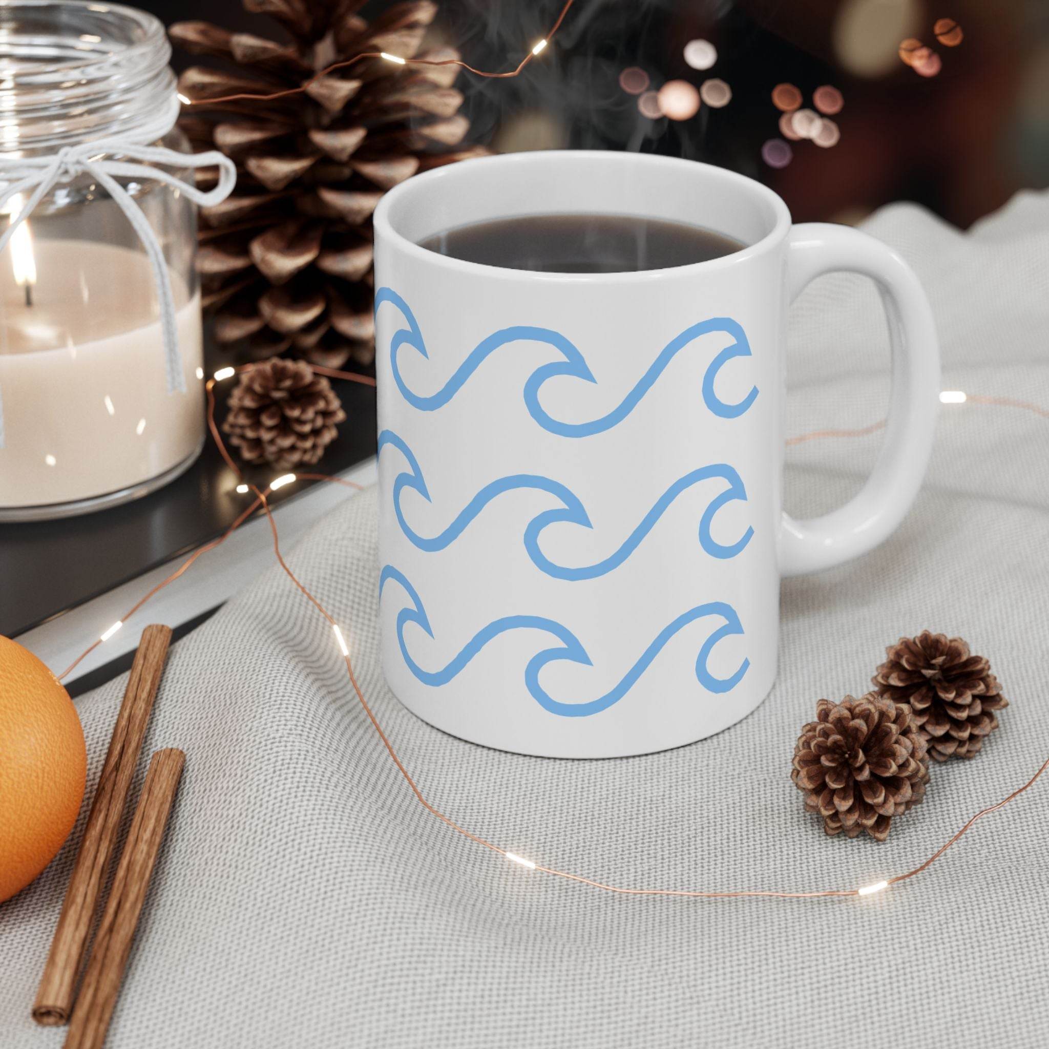 White ceramic mug with wave pattern filled with coffee on a cozy table setting with pine cones and candle