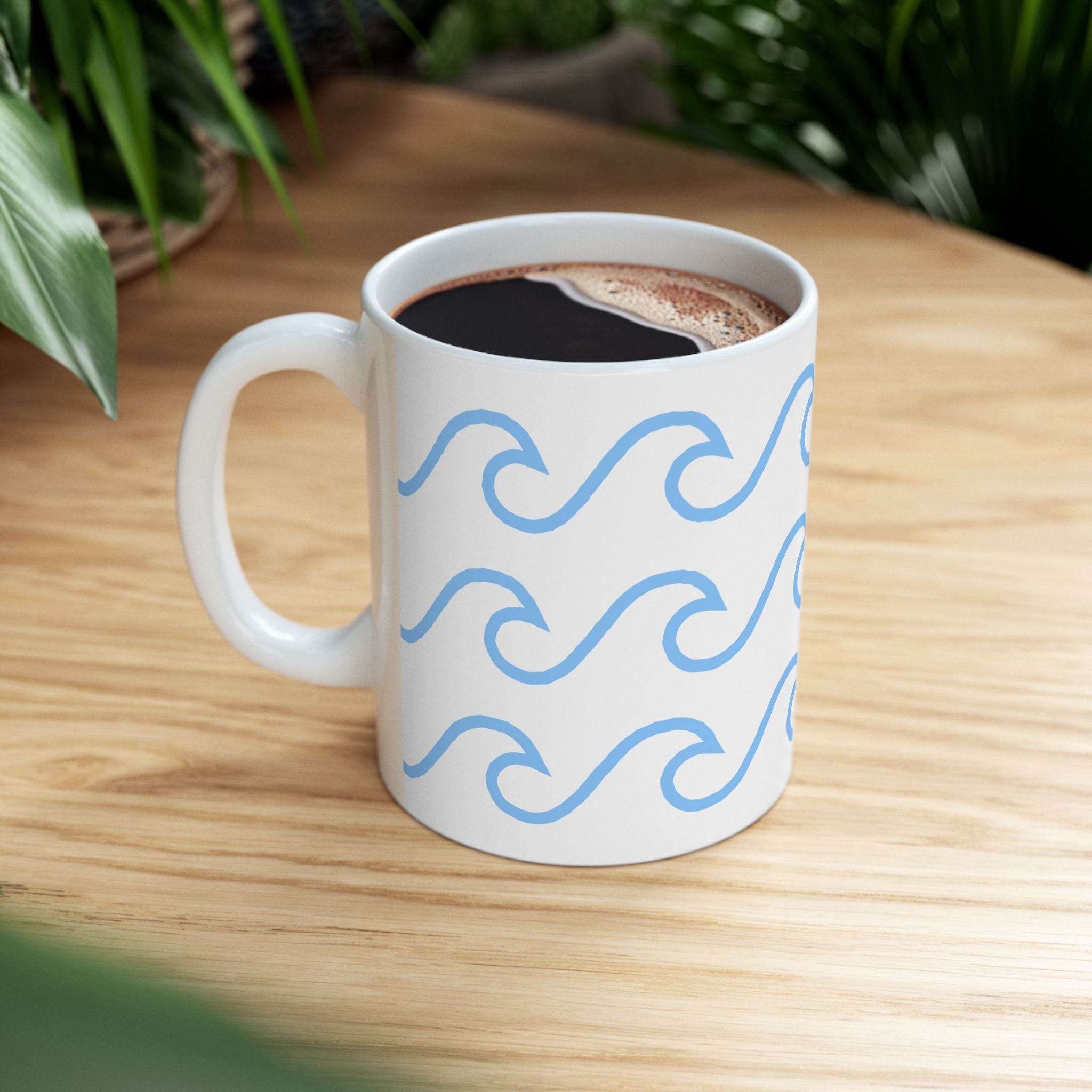 White ceramic mug with wave pattern in blue filled with coffee on wooden table