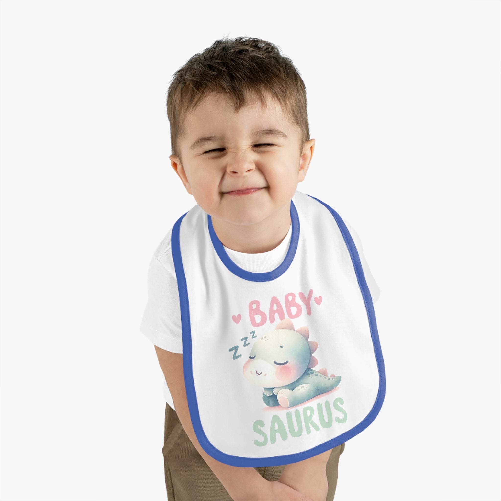 Smiling toddler wearing Printify dinosaur print baby bib with sleeping baby dinosaur design and blue trim