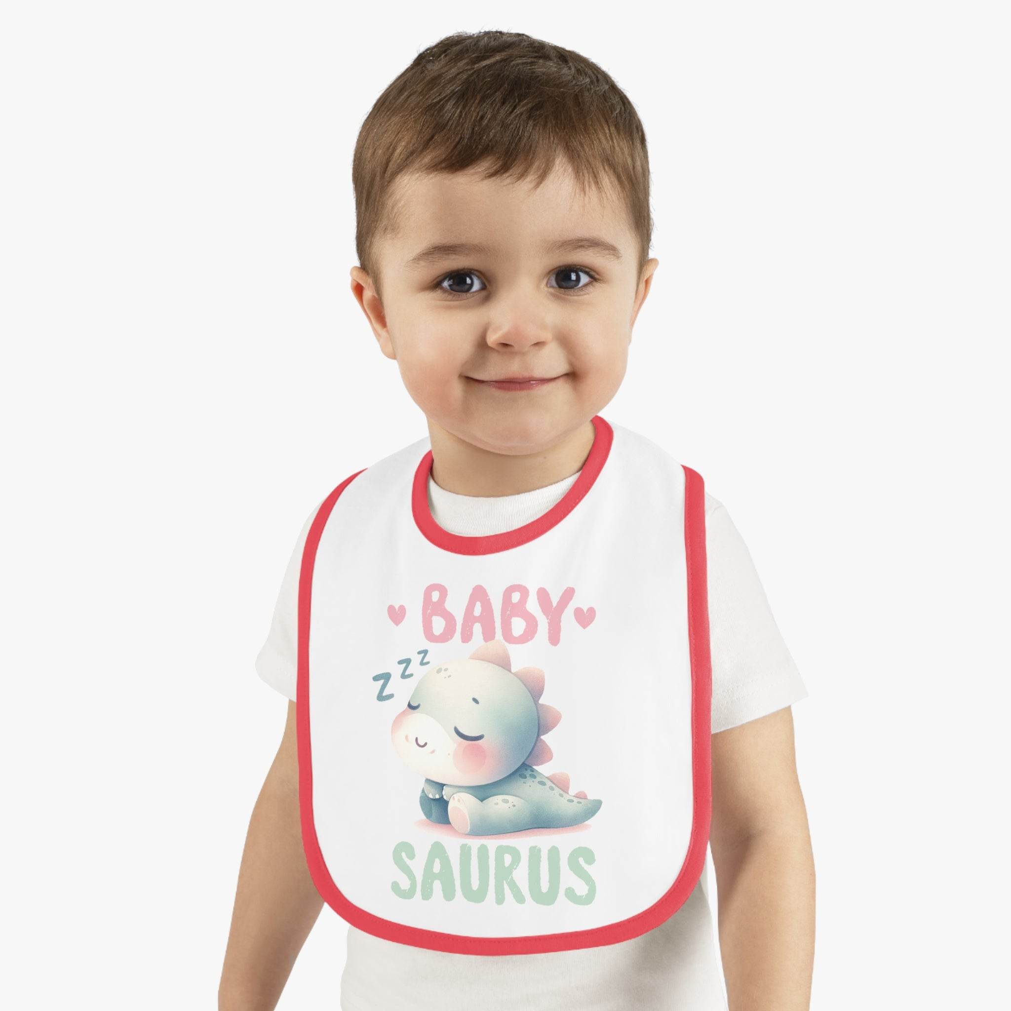 Smiling toddler wearing a dinosaur print baby bib with red trim from Printify