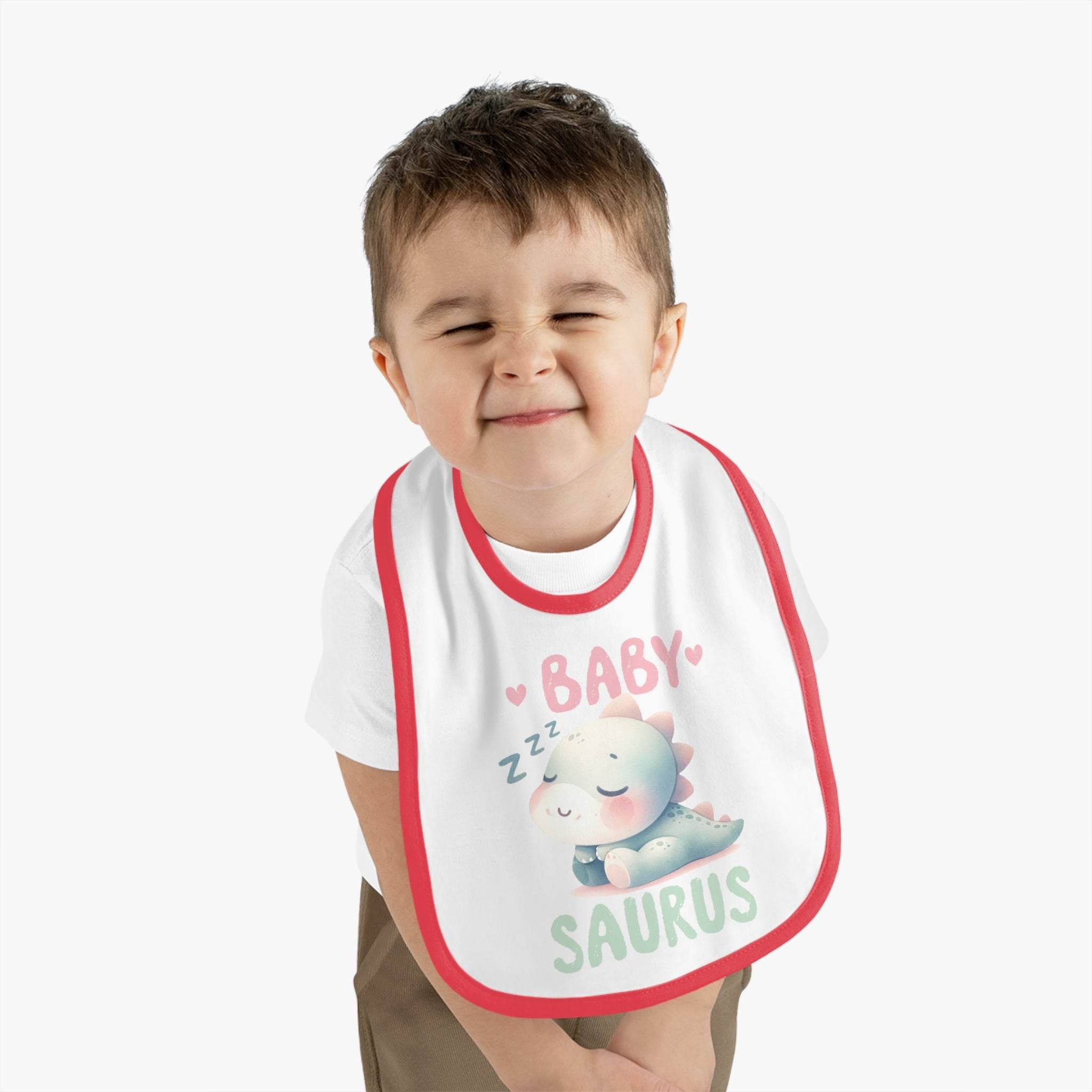 Cute toddler wearing a dinosaur print baby bib with a sleeping baby dinosaur design and red trim