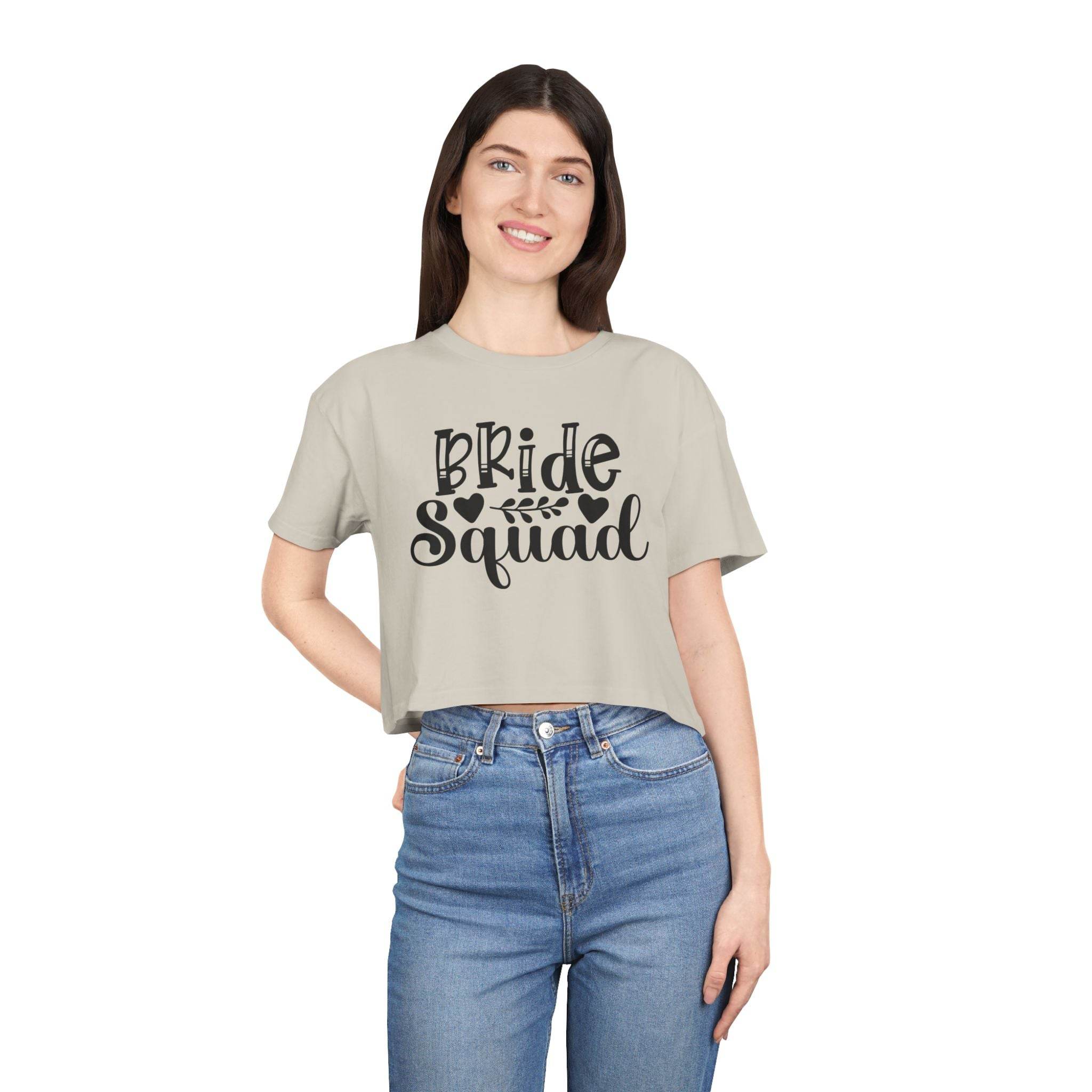 Smiling model wearing eco-friendly bride squad crop top in beige with black Bride Squad print paired with high waist jeans