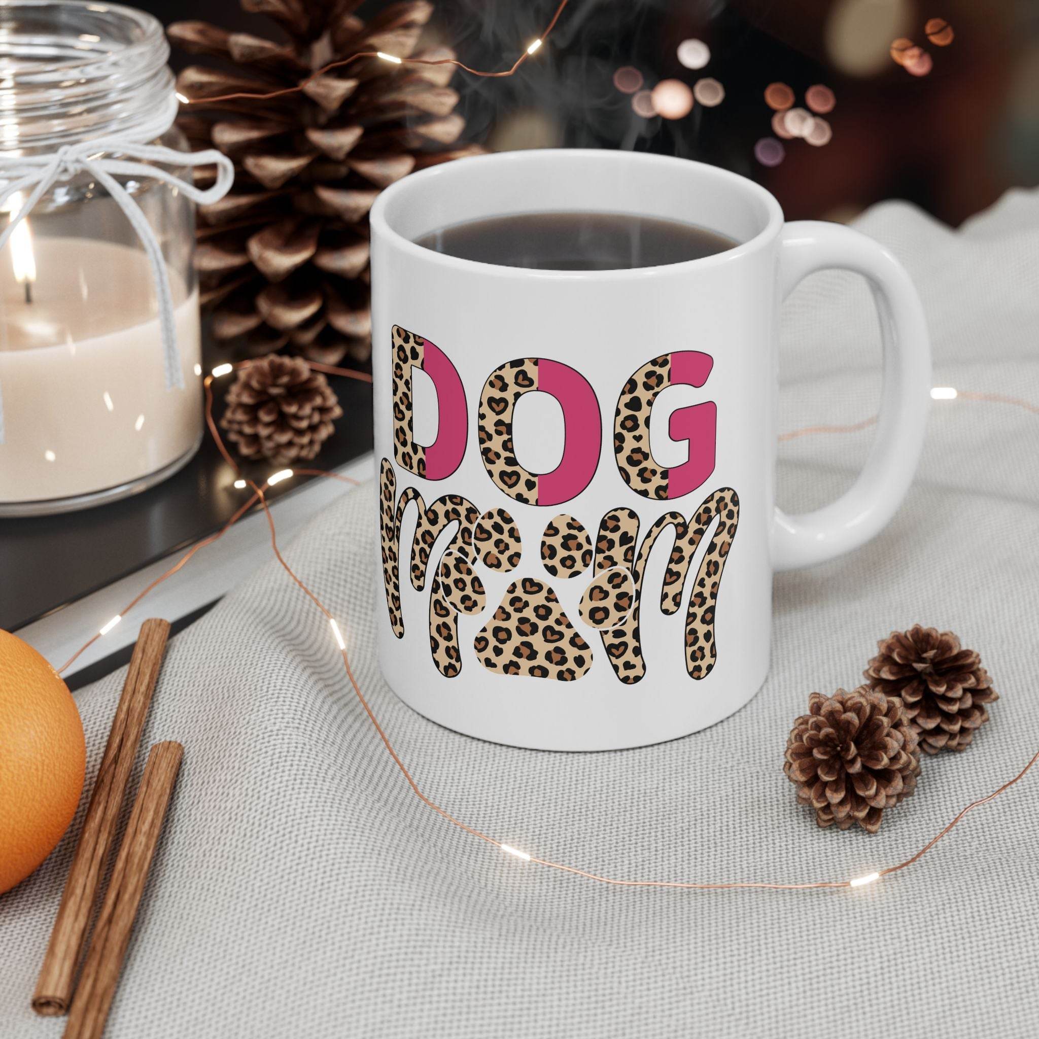 White eco friendly ceramic dog mom mug with leopard print DOG MOM text filled with coffee beside pinecones and candle holiday gift