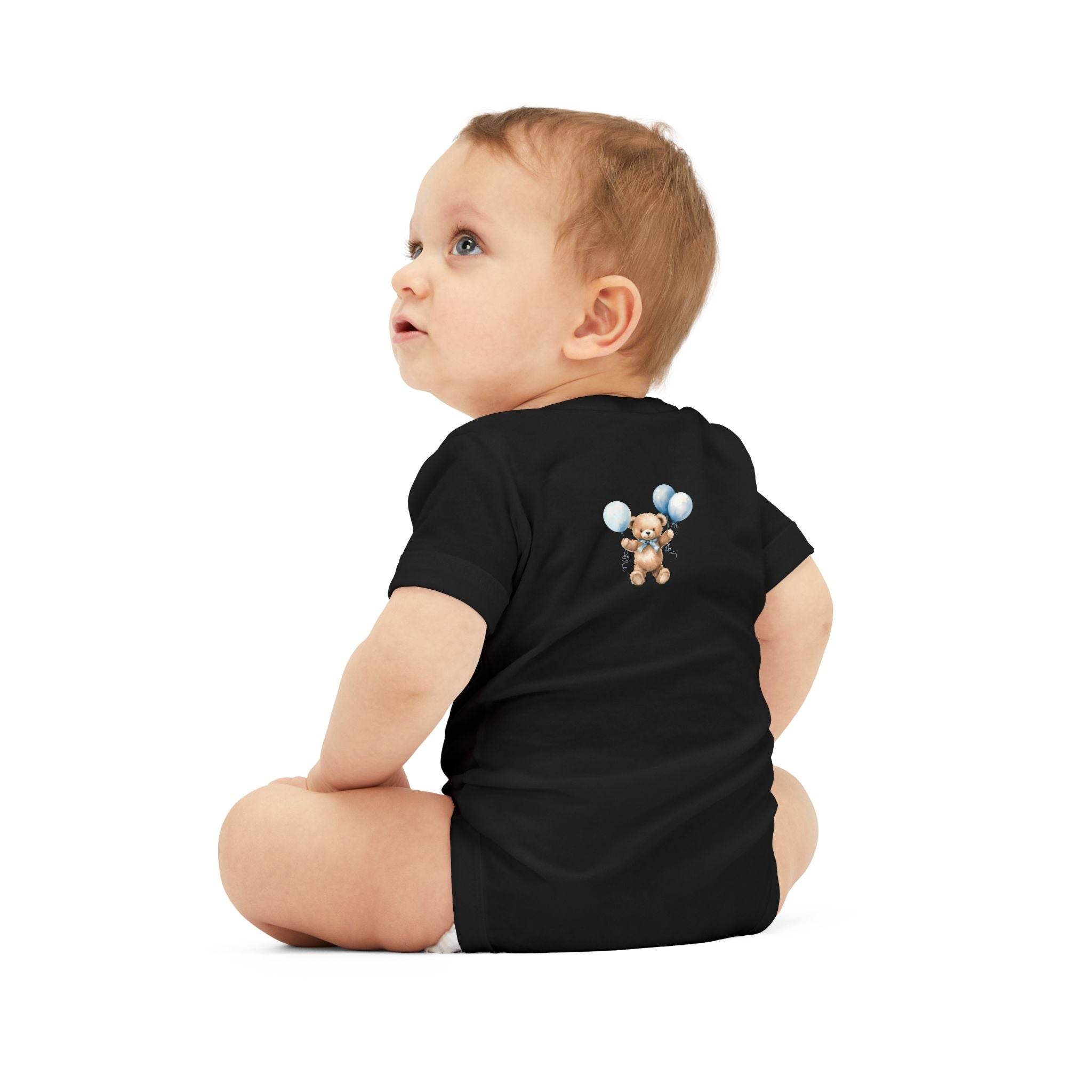 Baby wearing black eco-friendly baby onesie with teddy bear and balloon design sitting on white background