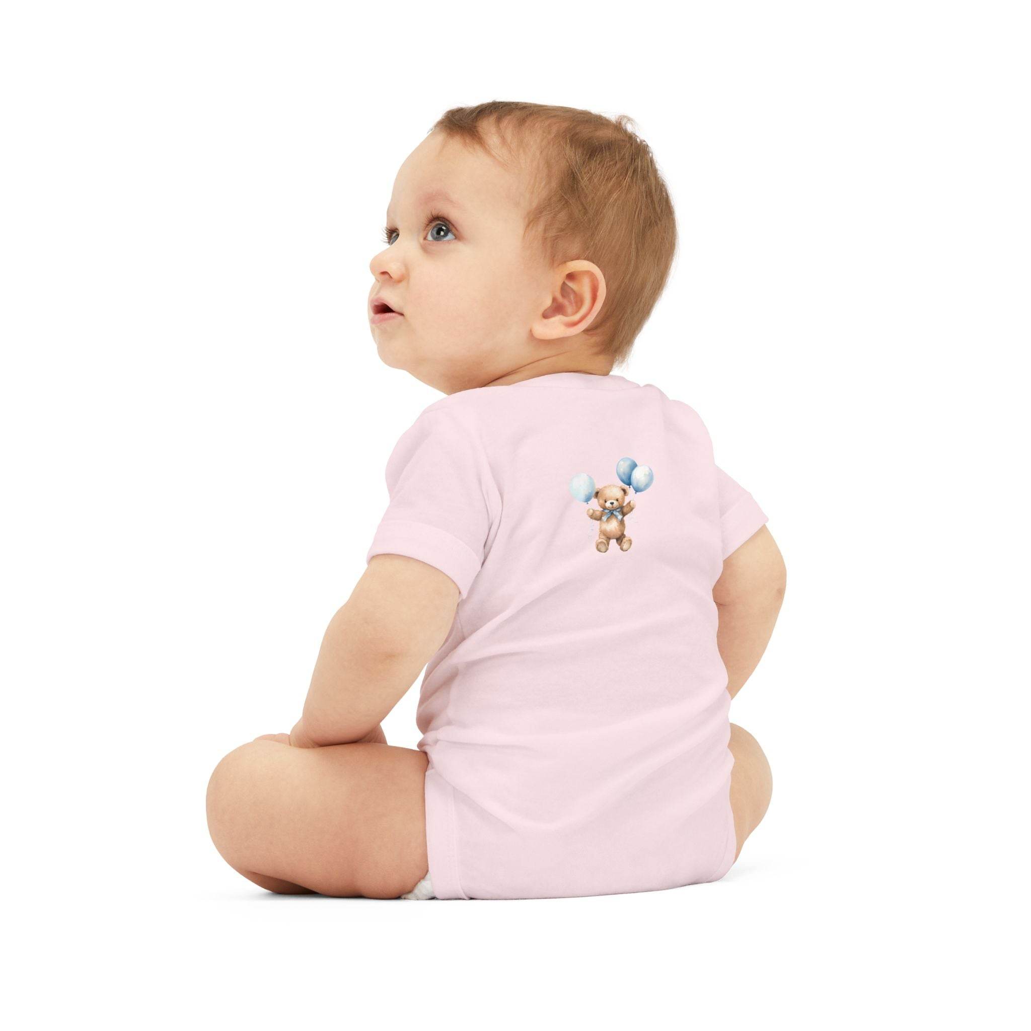 Baby wearing a pink eco-friendly baby onesie with teddy bear and balloons design sitting and looking up