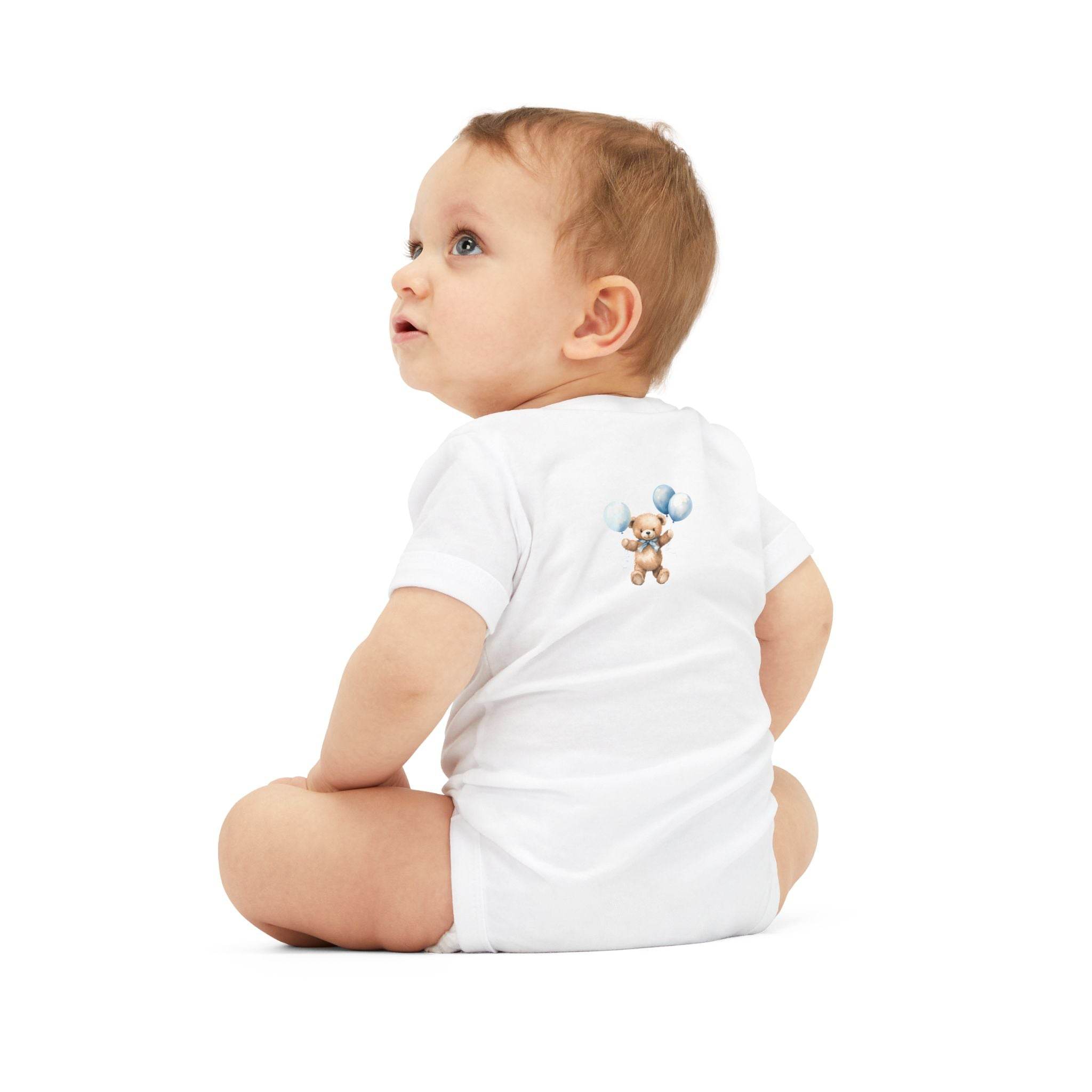 Baby wearing a white eco-friendly baby onesie with a teddy bear and balloons print sitting on white background
