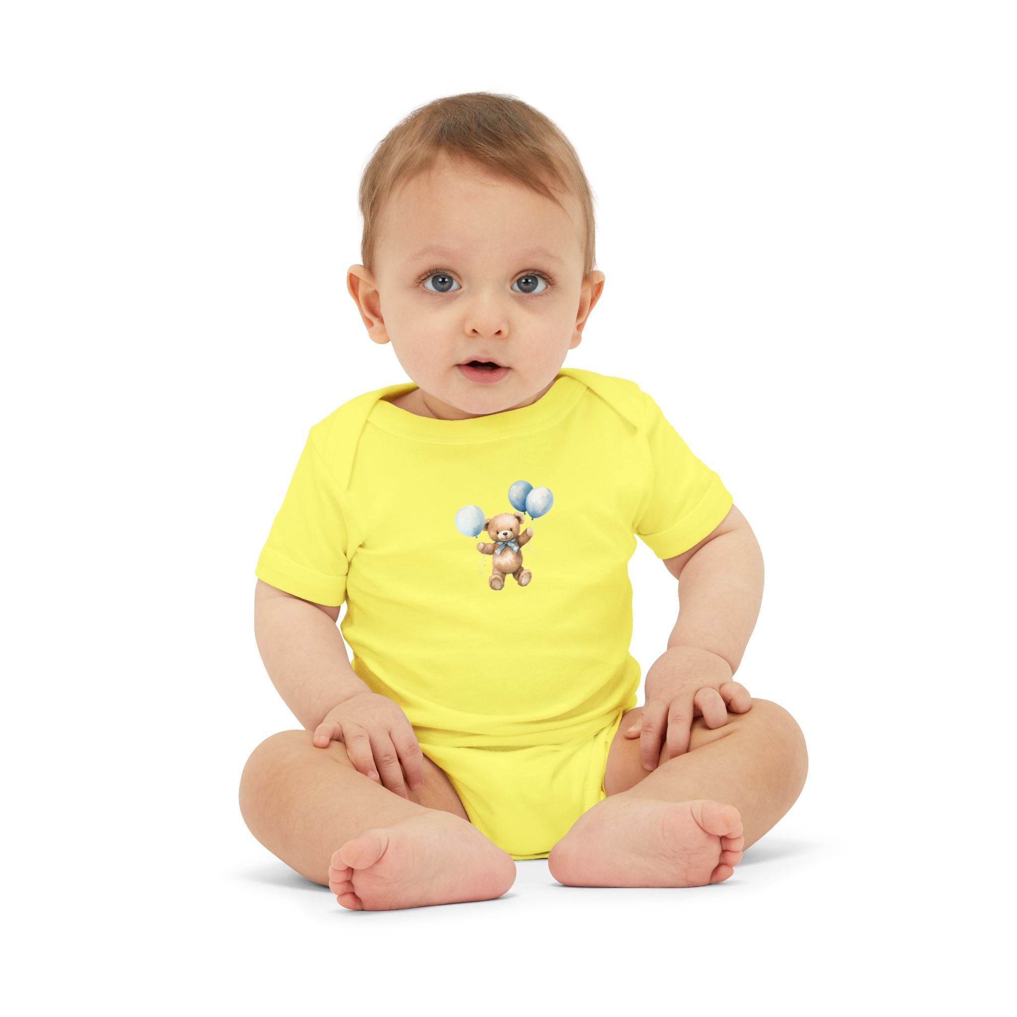 Baby wearing yellow eco-friendly baby onesie with teddy bear and balloons design sitting on white background