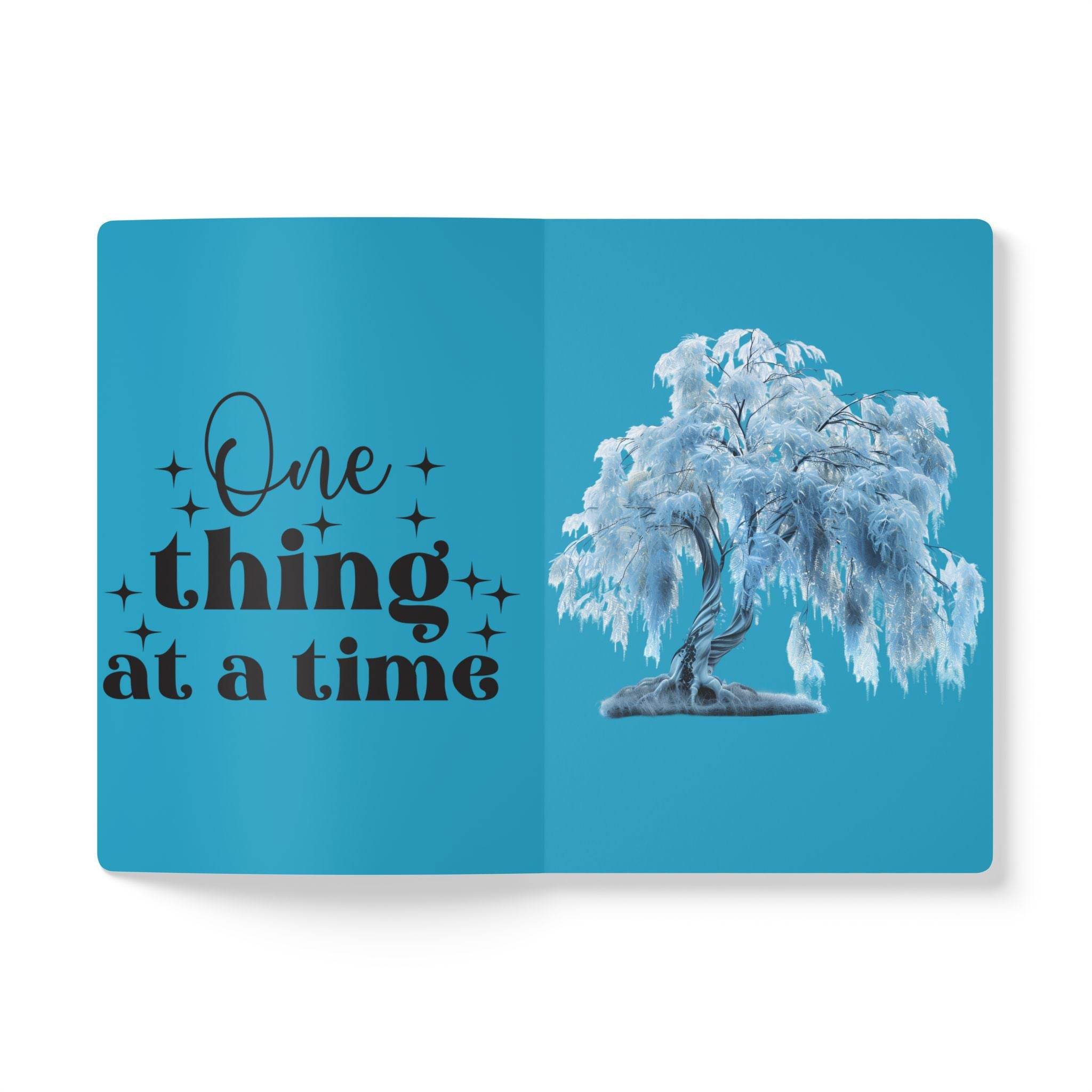 Open eco-friendly softcover journal with blue cover featuring one thing at a time quote and tree illustration