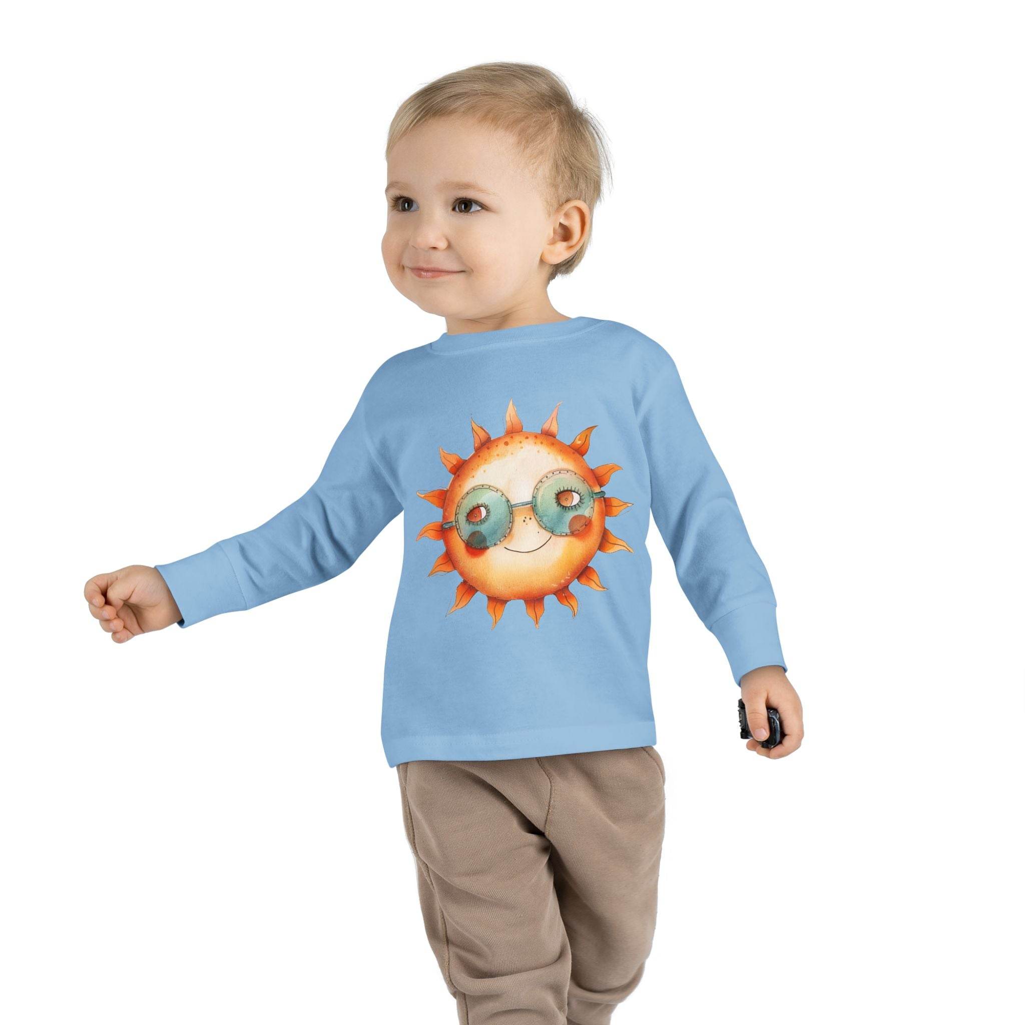 Toddler wearing a Printify eco-friendly toddler long sleeve shirt with sun graphic in light blue