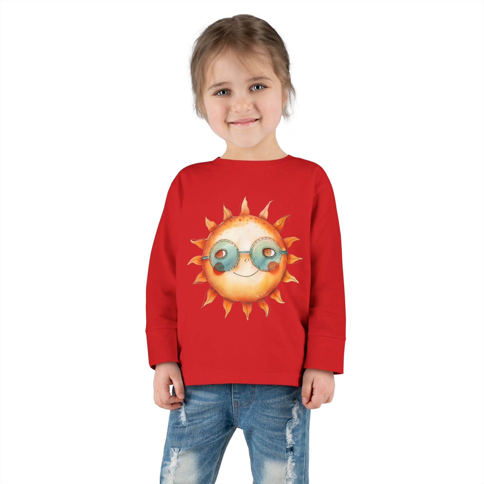 Child wearing a red eco-friendly toddler long sleeve shirt with a smiling sun graphic and sunglasses