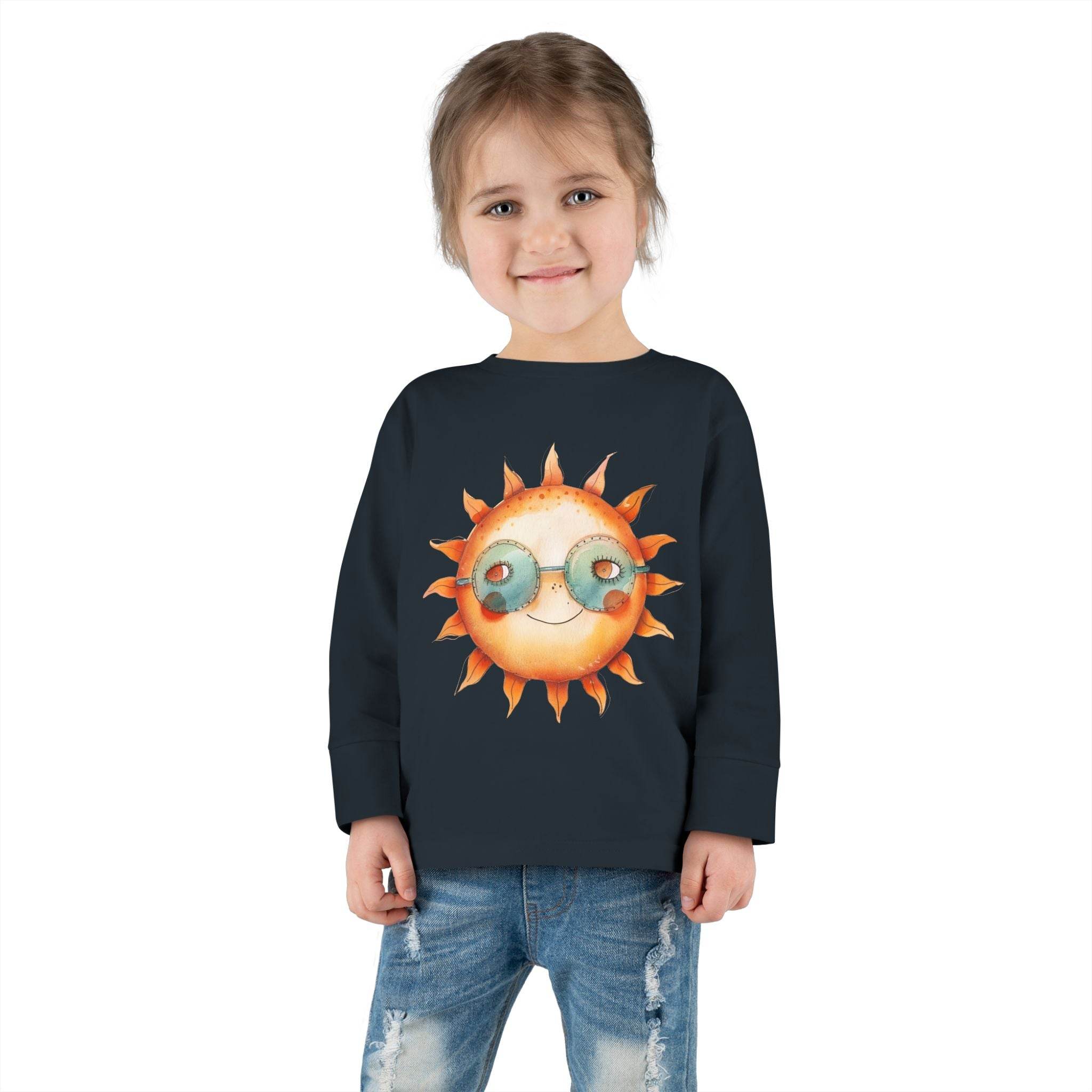 Toddler wearing a Printify eco-friendly toddler long sleeve shirt with sun graphic and sunglasses