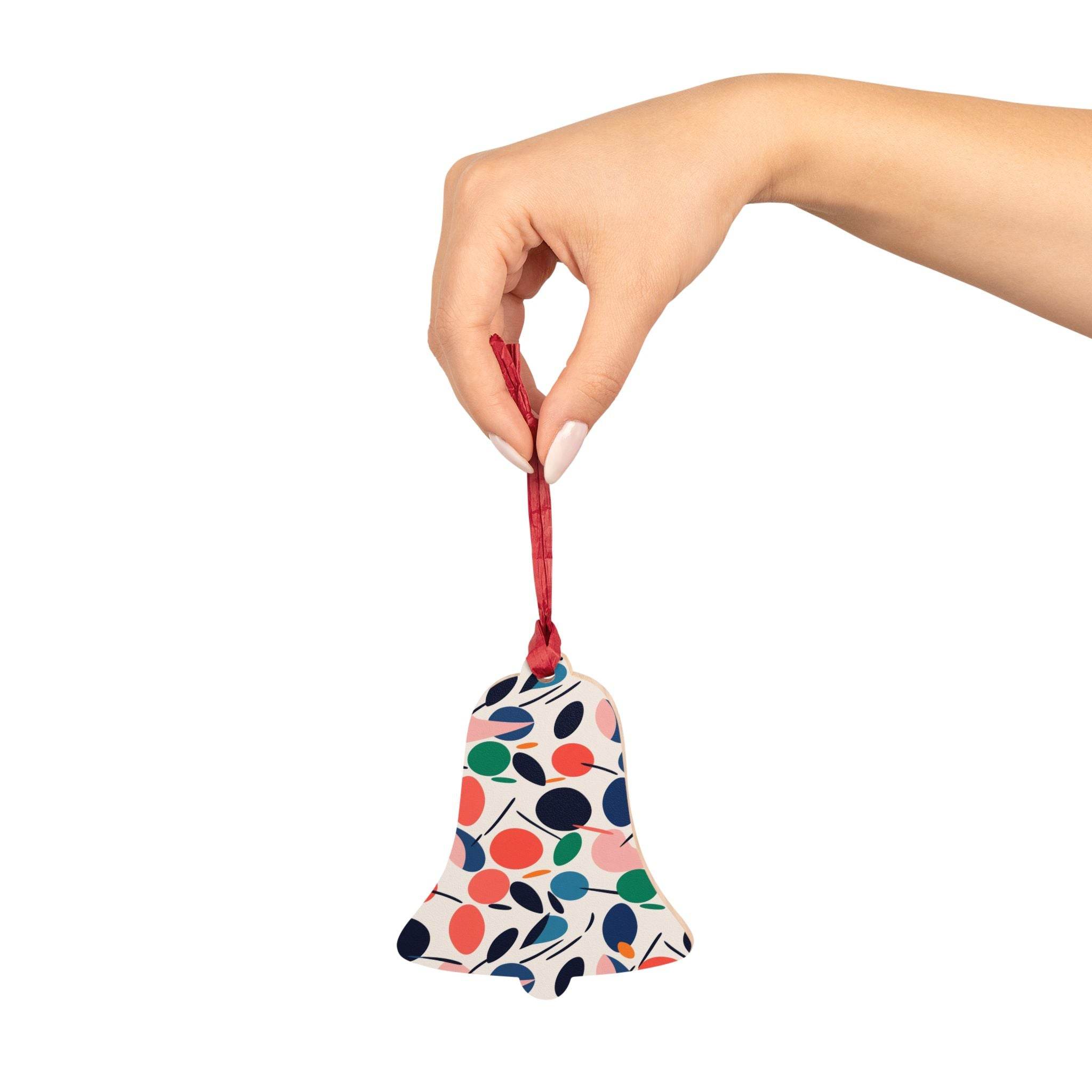 Hand holding eco-friendly wooden ornaments shaped like a bell with colorful berry pattern and red ribbon