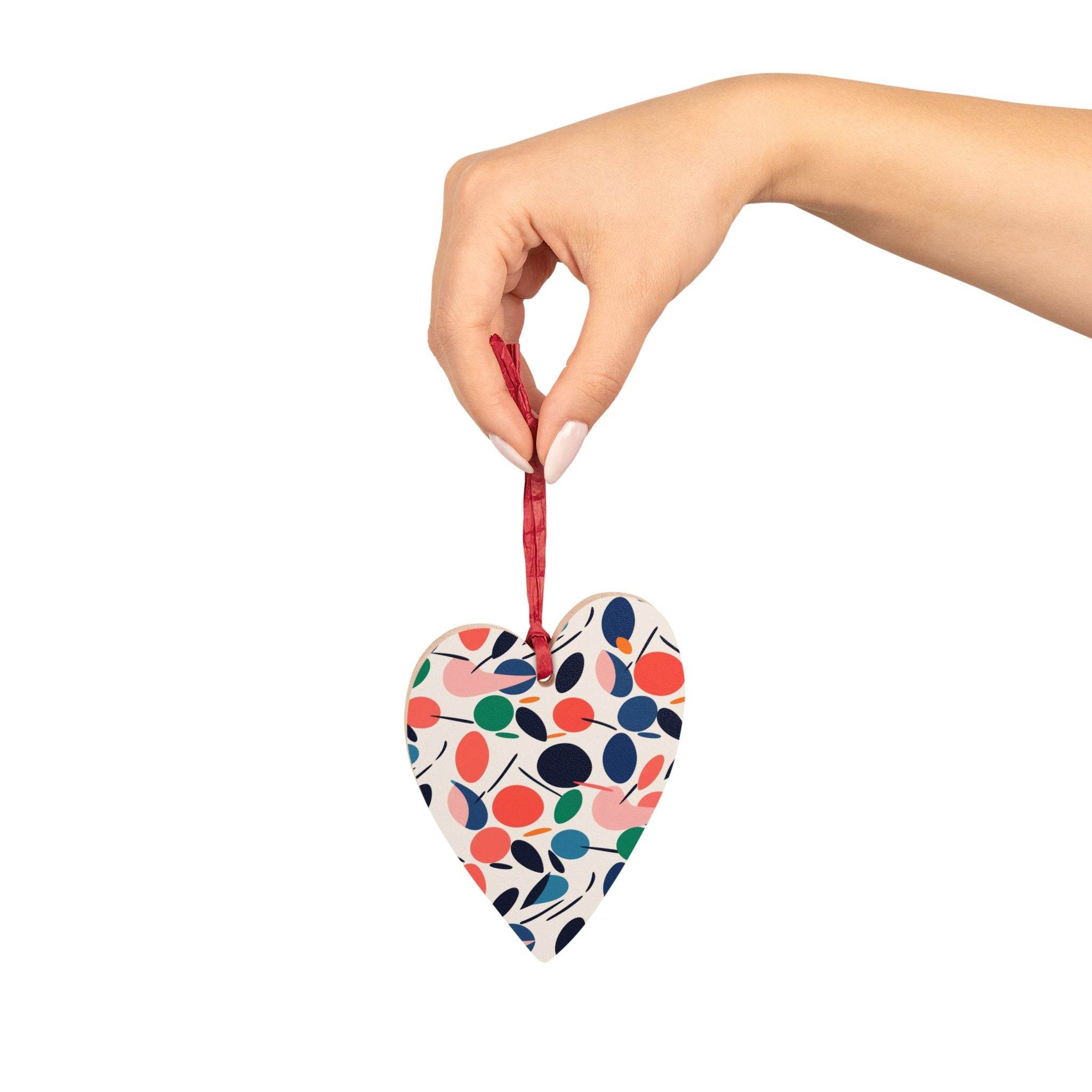 Hand holding eco-friendly wooden ornaments heart-shaped with colorful leaf pattern and red ribbon
