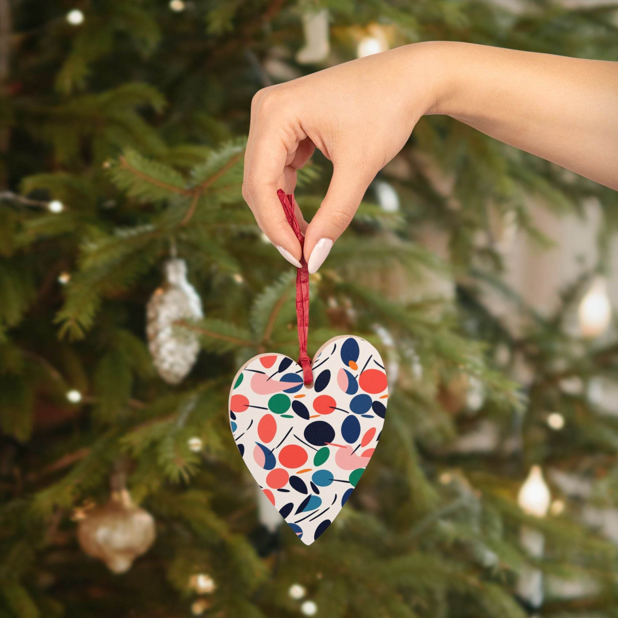 Hand holding eco-friendly wooden ornaments heart shaped with colorful leaf design near decorated Christmas tree