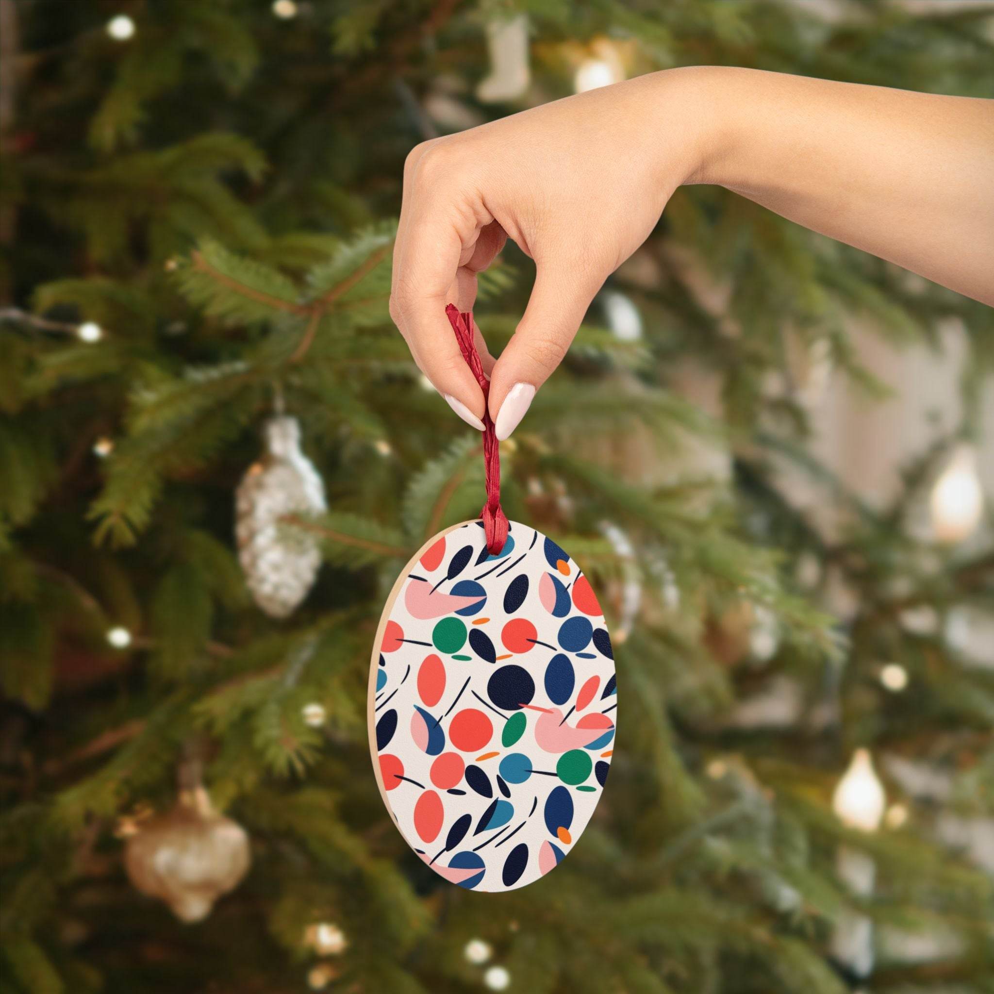 Hand holding eco-friendly wooden ornaments with colorful leaf pattern in front of decorated Christmas tree