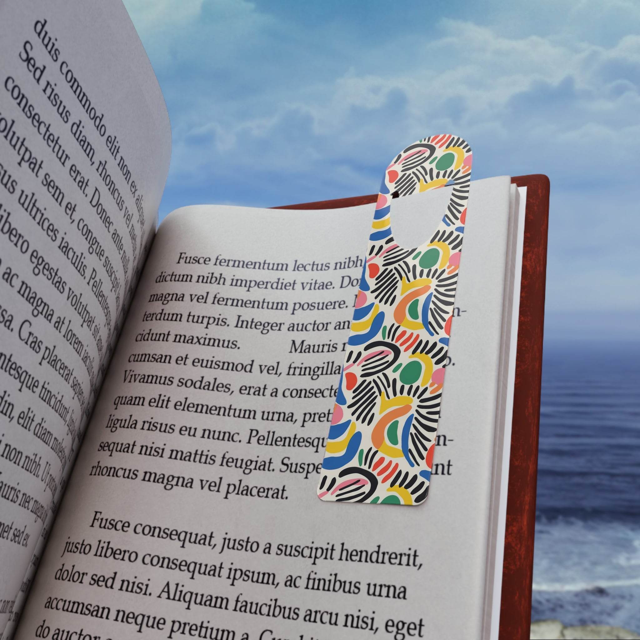 Printify eco-friendly art bookmark with colorful abstract design placed in an open book near the ocean