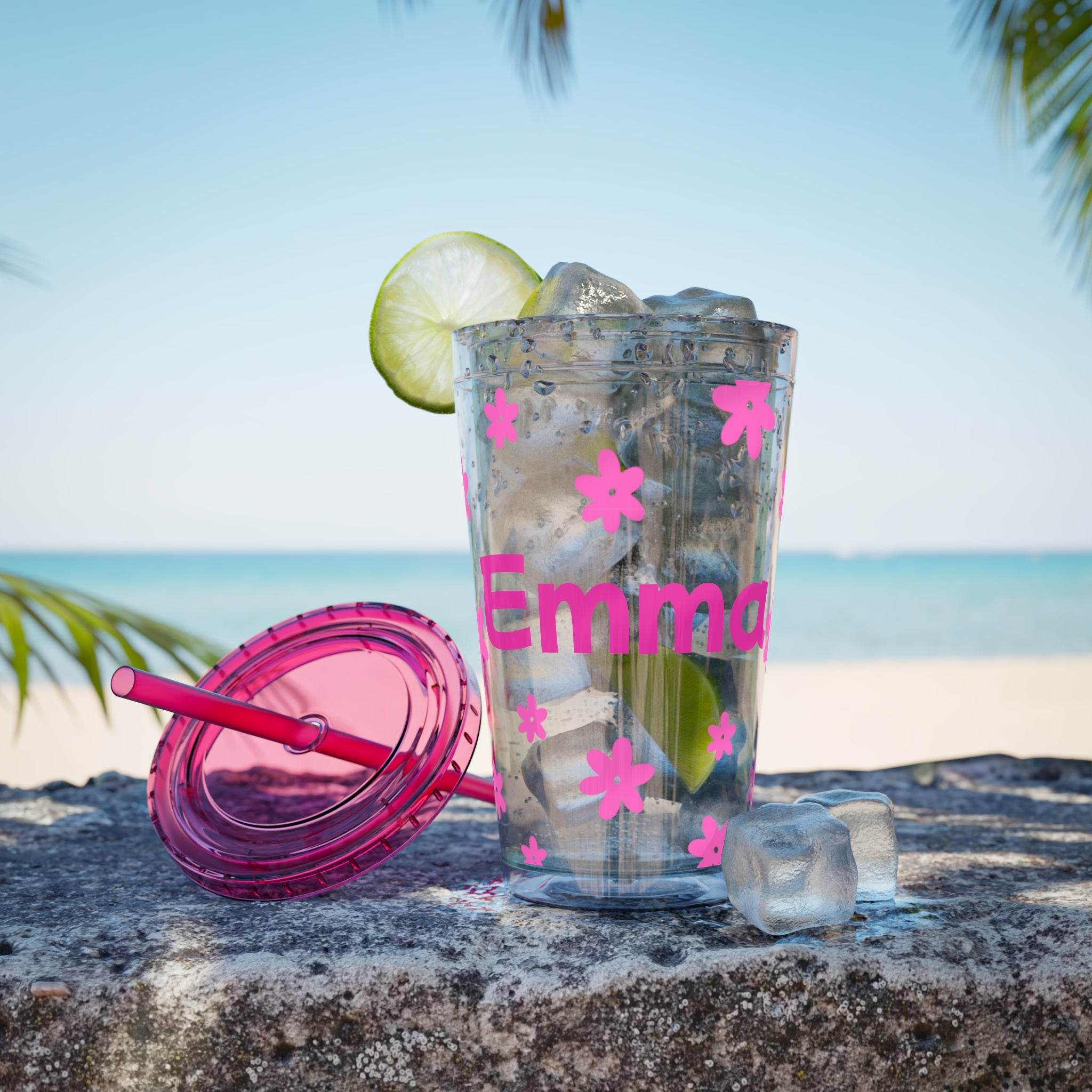 Clear personalized eco-friendly tumbler with pink floral decals and name Emma filled with ice and lime on a beach with pink lid