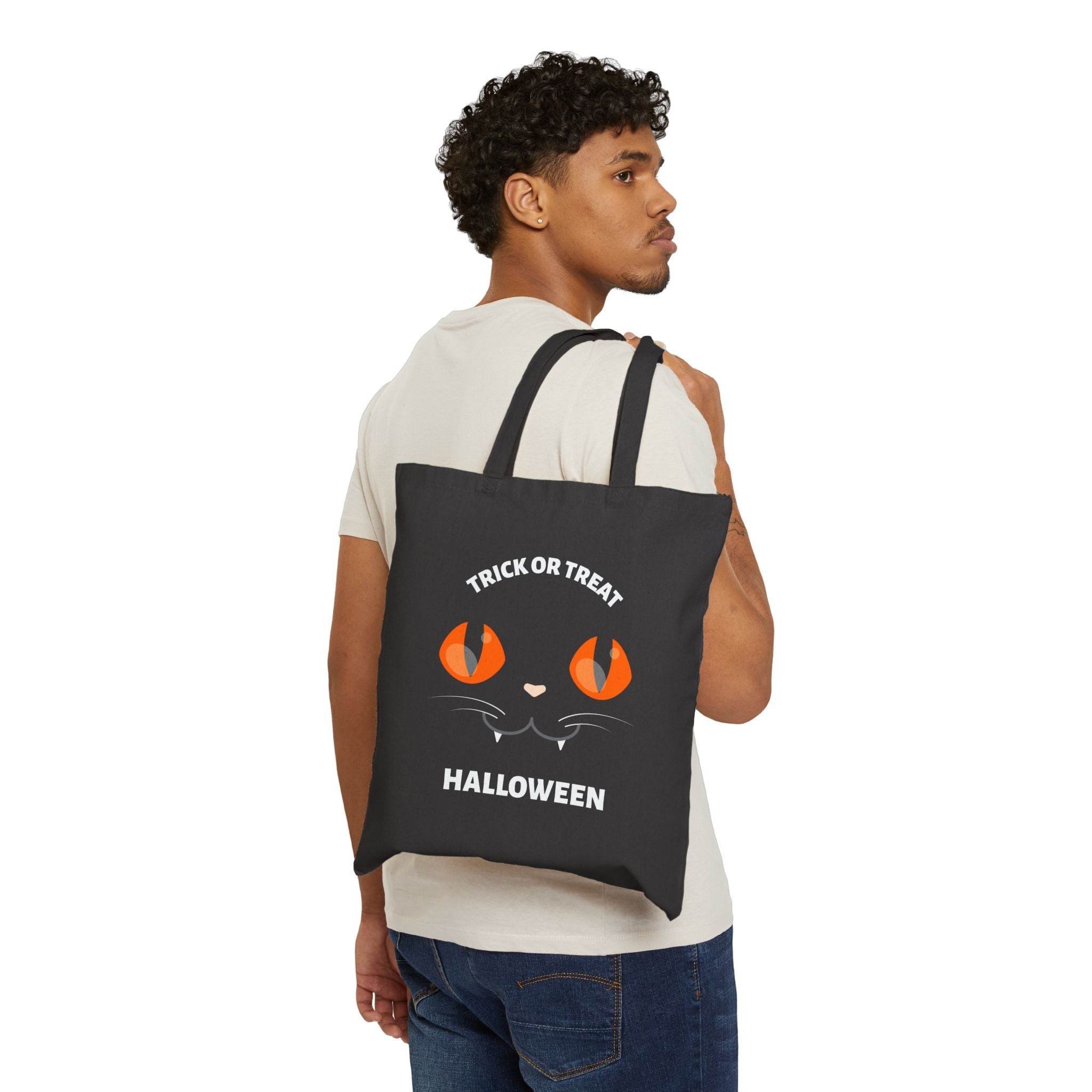 Man carrying Printify black eco-friendly Halloween tote bag with orange cat eyes and trick or treat text
