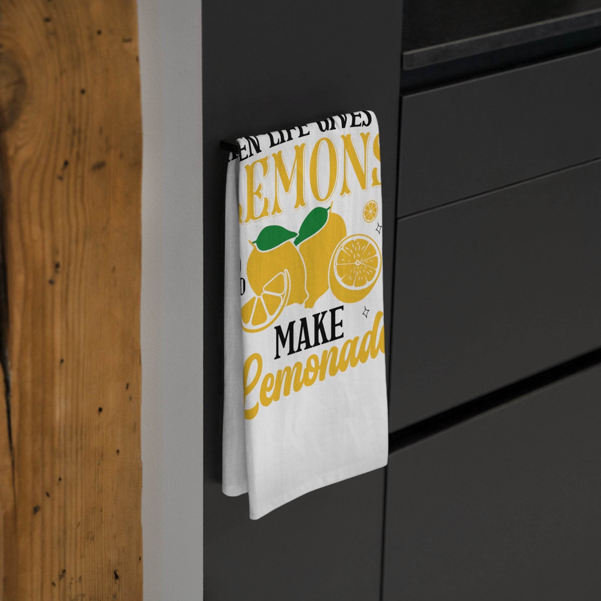 Printify lemonade themed tea towel with yellow lemon design hanging on black kitchen cabinet