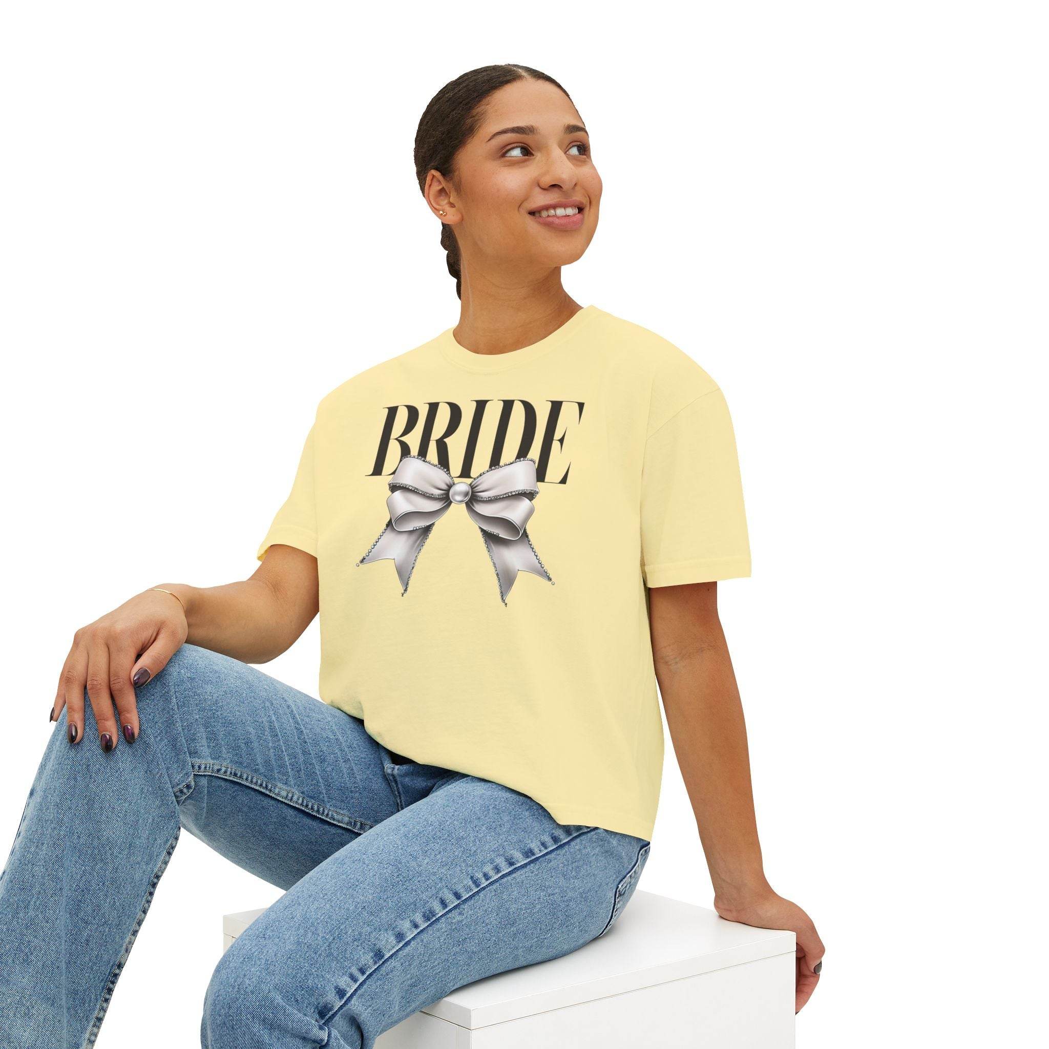 Printify model wearing pale yellow eco-friendly bridal t-shirt with BRIDE text and silver bow styled with jeans