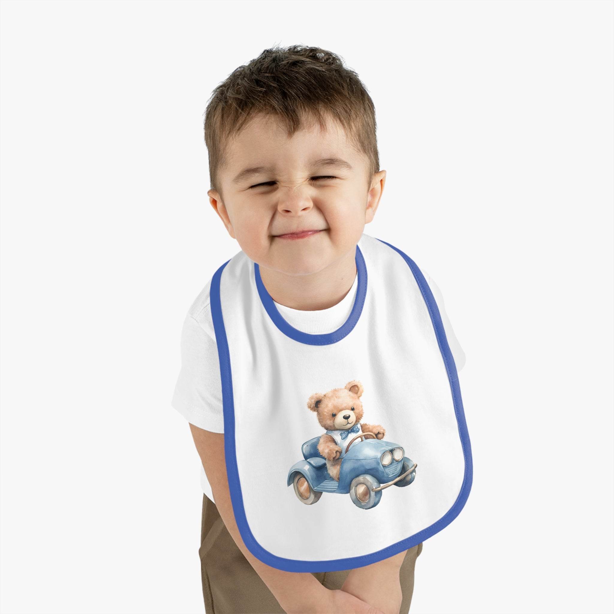 Toddler wearing a Printify sustainable baby bib with a blue trim and teddy bear driving a car design