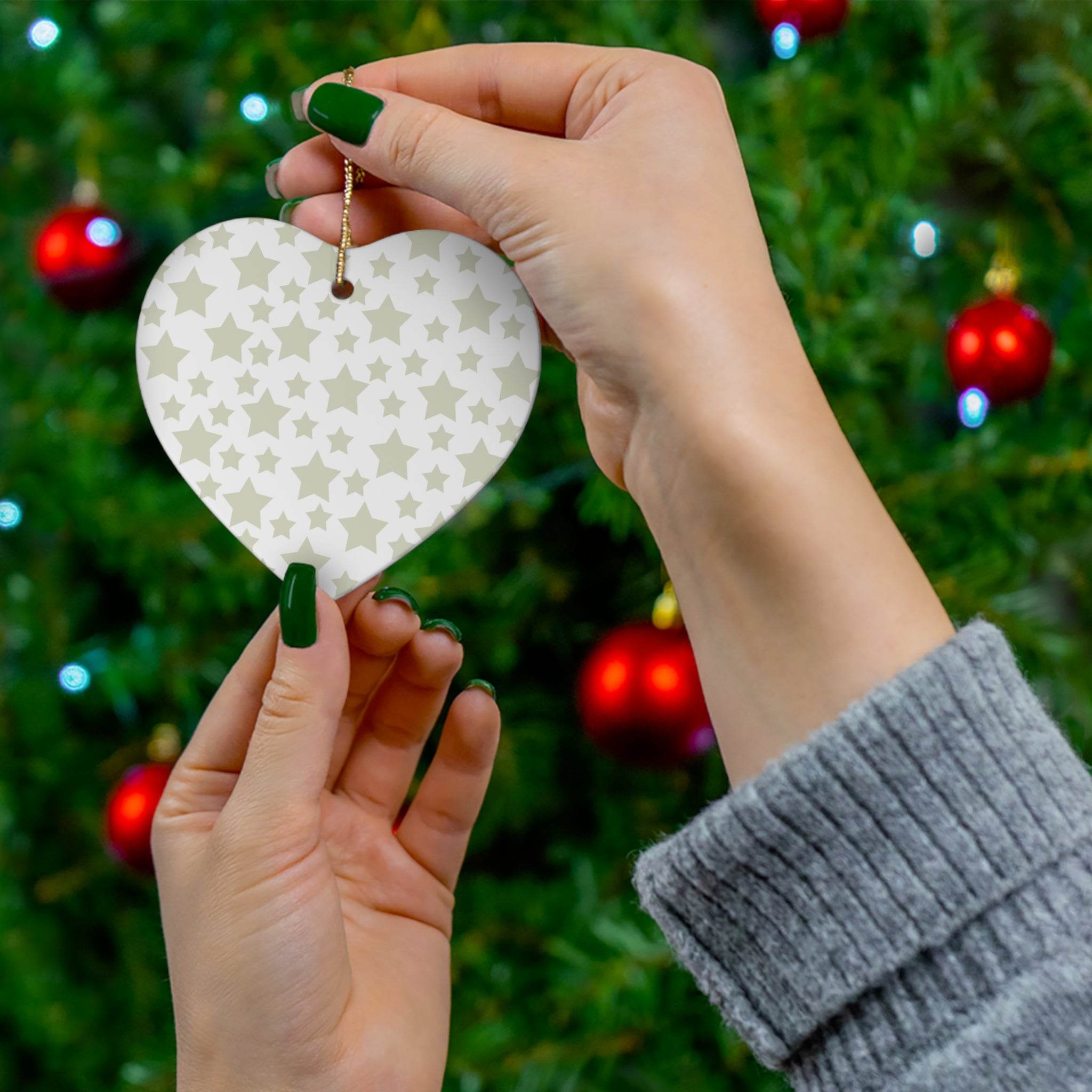 Hands holding heart-shaped twinkling stars holiday decoration against Christmas tree with red ornaments