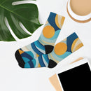 Printify eco-friendly recycled socks with colorful blue and yellow abstract pattern laid flat with tablet and plant