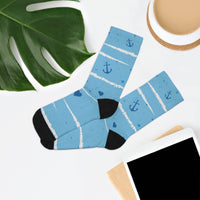 Blue recycled poly socks with anchor and heart patterns displayed next to a green leaf and tablet