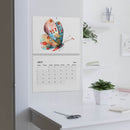 Printify butterfly design 2025 calendar hanging on wall above white desk with plant and scissors