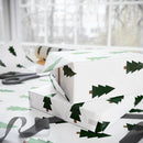 Christmas tree wrapping paper with green tree prints used to wrap gifts near scissors and ribbon