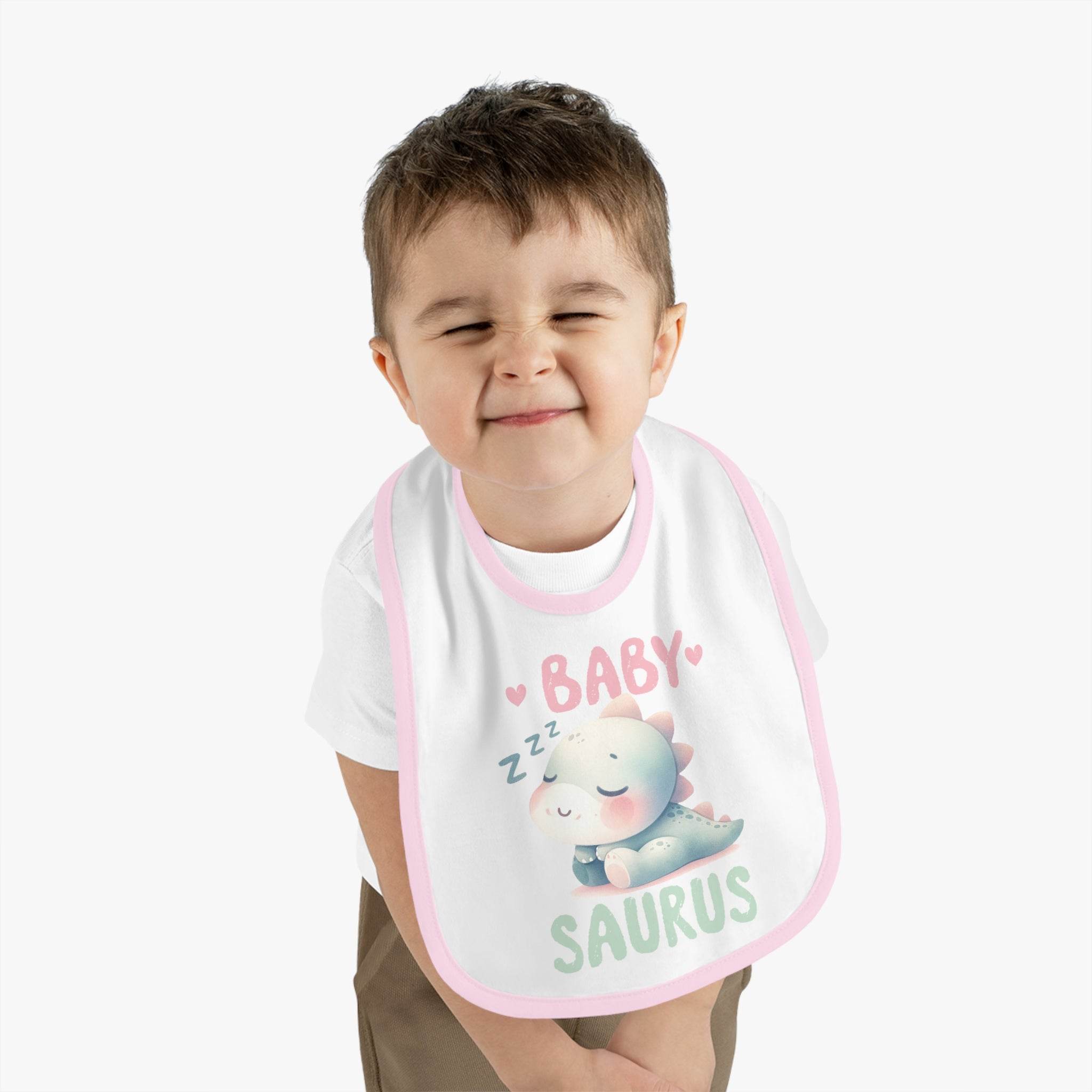 Toddler wearing a dinosaur print baby bib with sleeping dinosaur design and pink trim