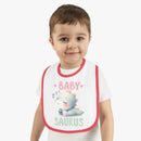 Smiling toddler wearing a dinosaur print baby bib with red trim from Printify