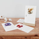 Eco-friendly 2025 desk calendar with dragon illustrations on wooden table by Printify