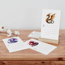 Printify eco-friendly 2025 desk calendar with dragon artwork on wooden stand and loose calendar pages on wood surface