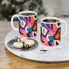 Printify eco-friendly ceramic mugs with colorful abstract design filled with steaming coffee on marble tray with cookies