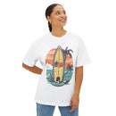 Woman wearing a Printify eco-friendly oversized t-shirt with a surfboard and tropical sunset graphic
