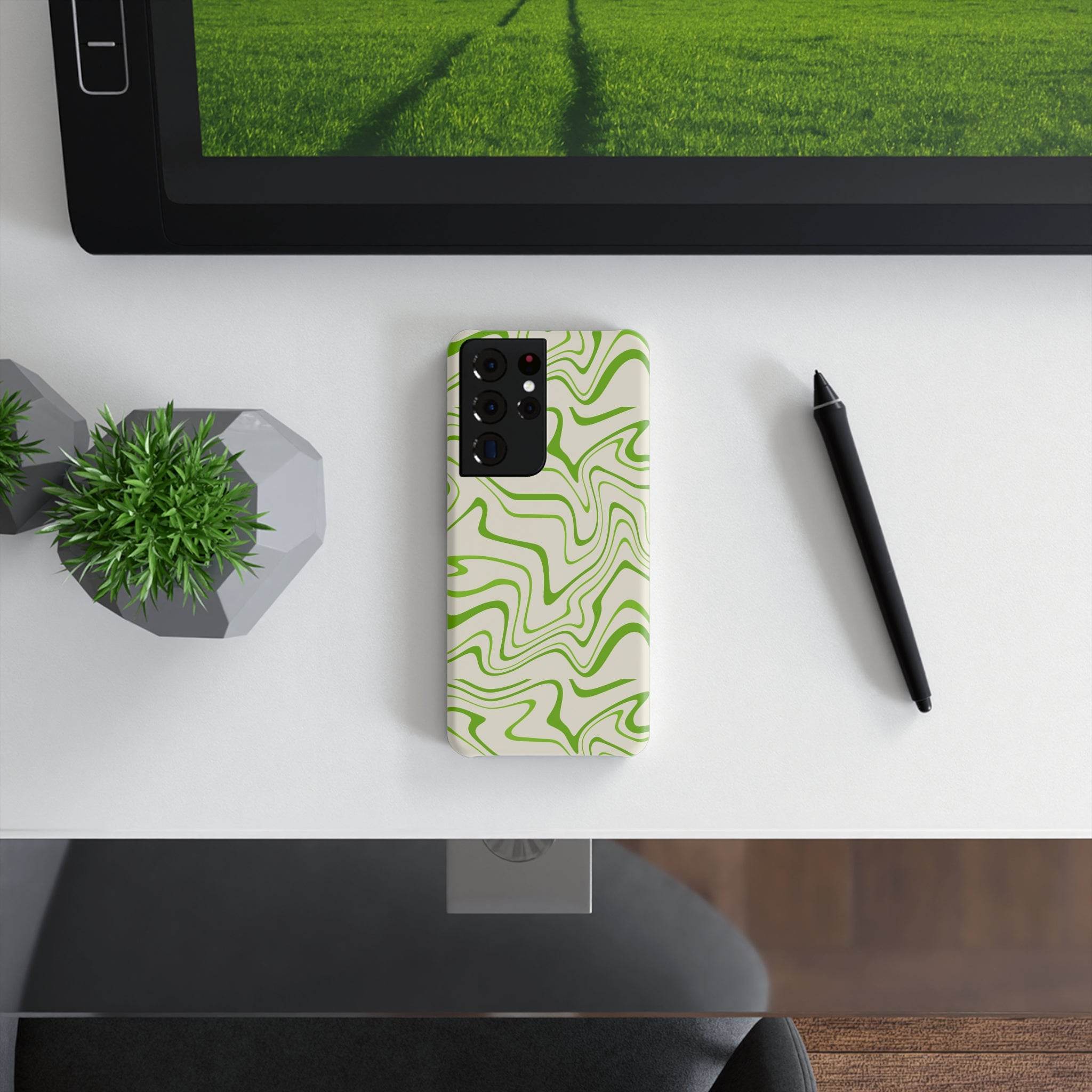 Printify eco-friendly phone case with green abstract design placed on white desk next to pen and small plant