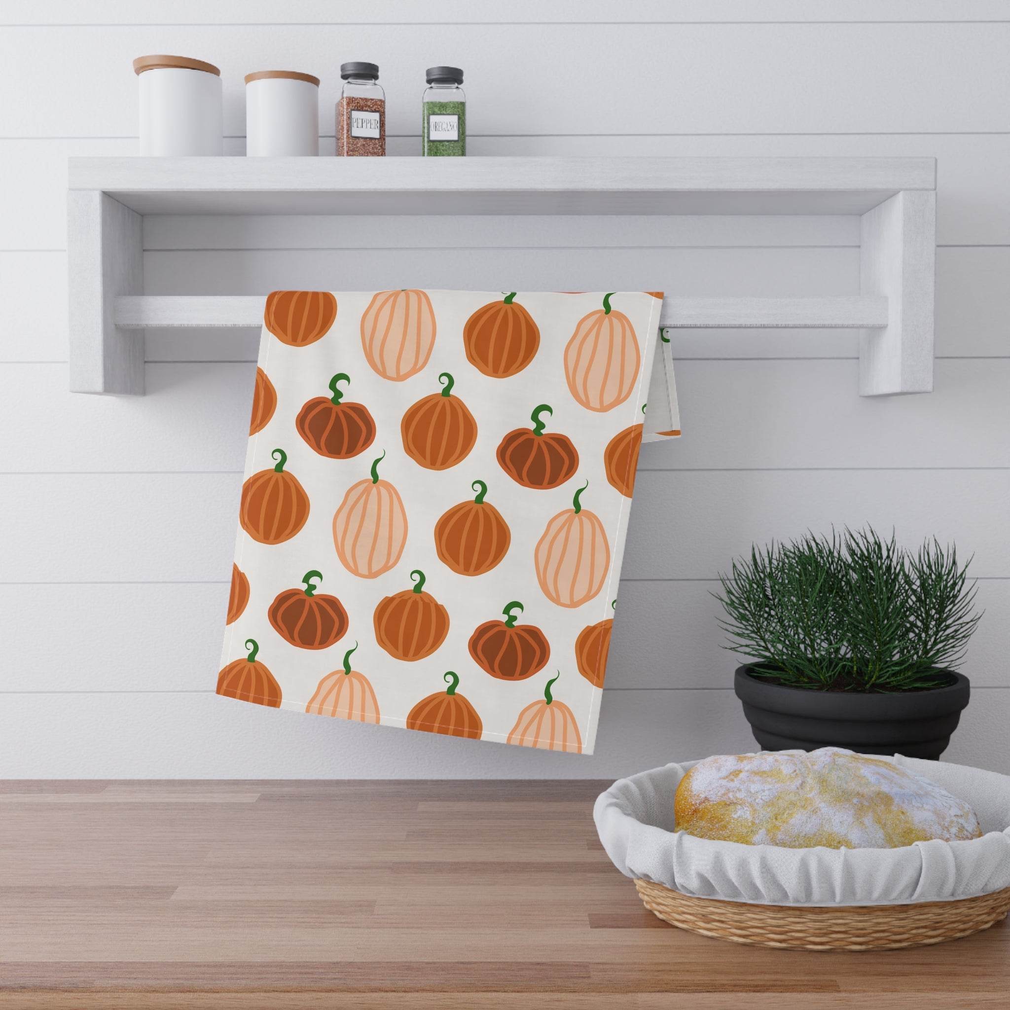 Printify eco-friendly pumpkin tea towels hanging on white kitchen shelf with spice jars and bread basket