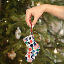 Hand holding colorful eco-friendly wooden ornaments shaped like a Christmas stocking by a decorated tree