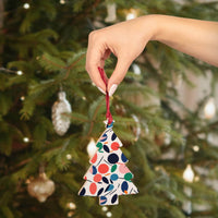 Hand holding eco-friendly wooden ornaments shaped like Christmas tree with colorful abstract patterns