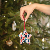 Hand holding eco-friendly wooden ornaments star with colorful leaf design in front of decorated Christmas tree