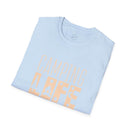 Printify folded light blue t shirt with CAMPING LIFE peach graphic of trees and campfire eco-friendly camping t-shirt