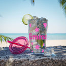 Clear personalized eco-friendly tumbler with pink floral decals and name Emma filled with ice and lime on a beach with pink lid