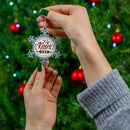 Hand holding pewter holiday decoration snowflake with Kisses and Wishes text in front of Christmas tree