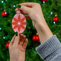Hands holding red flower patterned sustainable ceramic decor ornament in front of a decorated Christmas tree