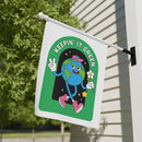 Sustainable house flags by Printify featuring a cartoon Earth with keepin' it green text hanging outside a home