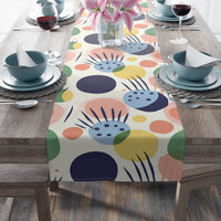 Printify eco-friendly table runner with colorful abstract shapes on a wooden dining table set with dishes and wine glasses